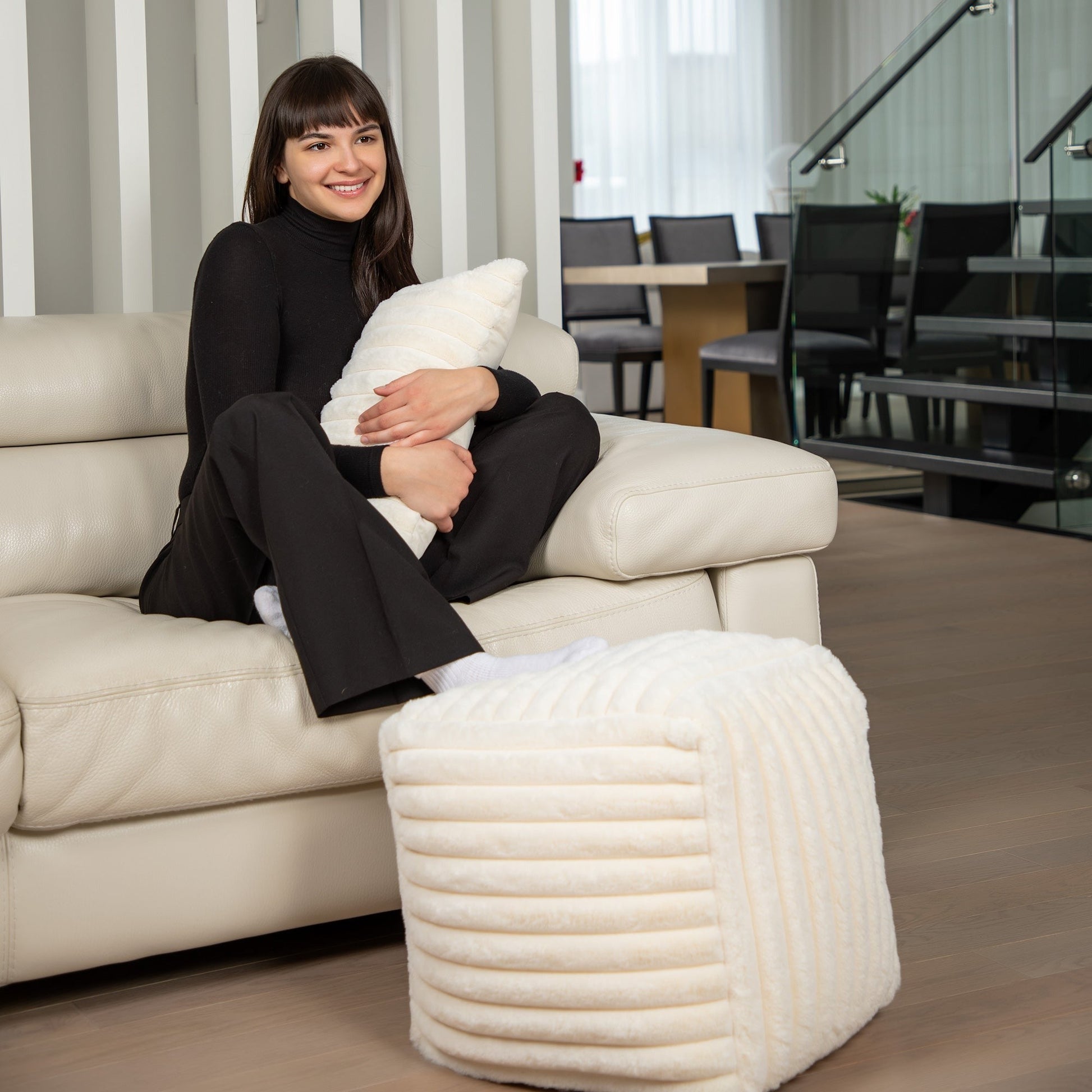 Woman sitting on a beige sofa holding a white pillow in a modern office setting.