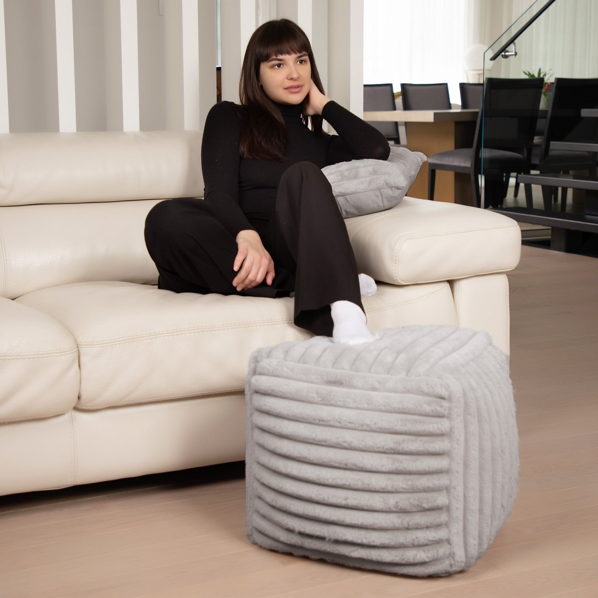 Woman sitting on a beige sofa with a textured gray ottoman in a modern living room.
