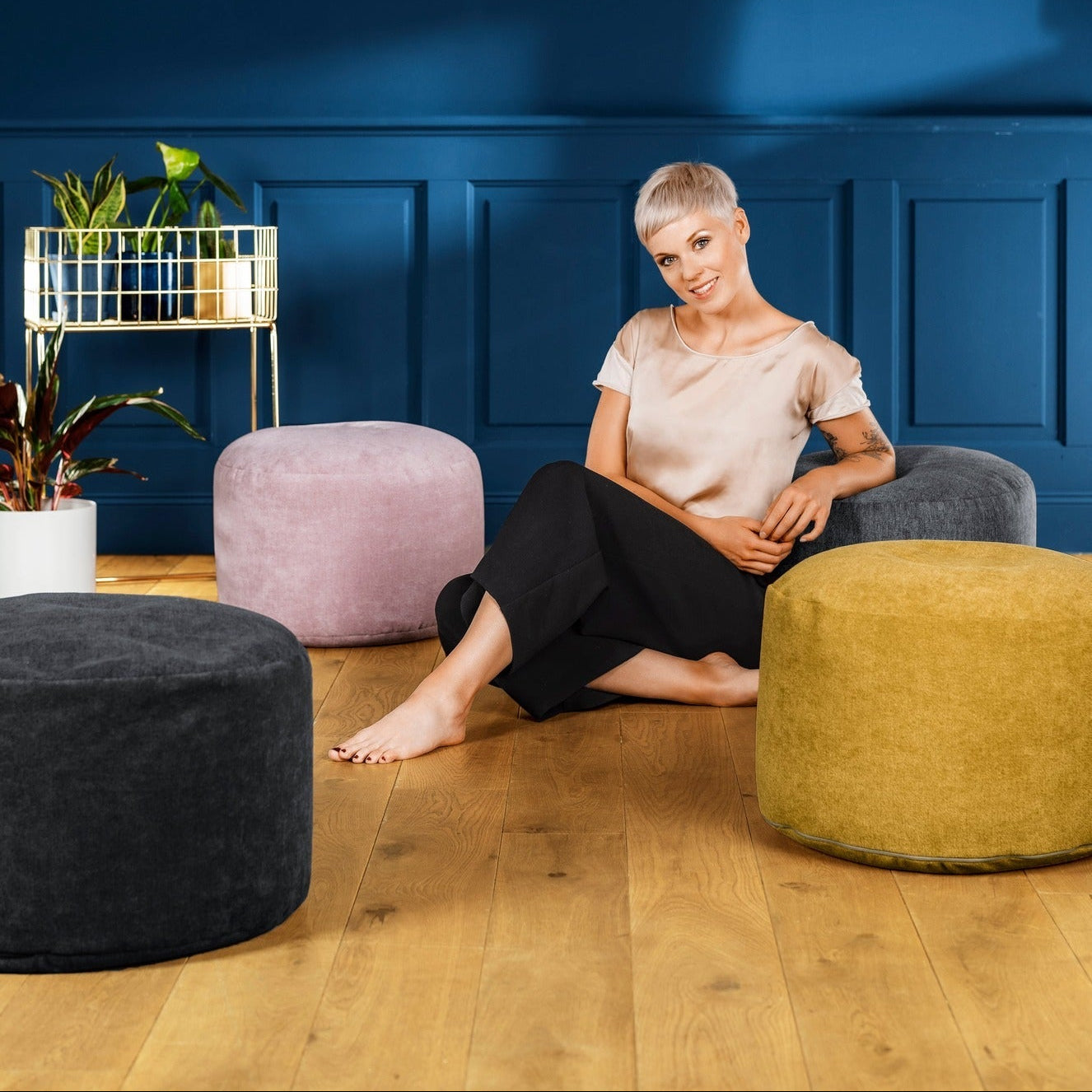 Woman sitting on a yellow pouf in a room with blue walls and various furniture pieces.
