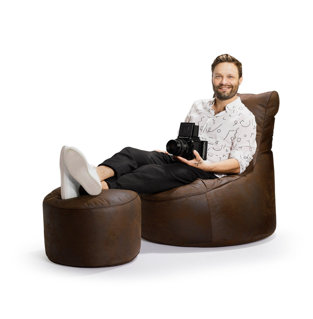 Man sitting on a brown bean bag chair with a camera, on a white background