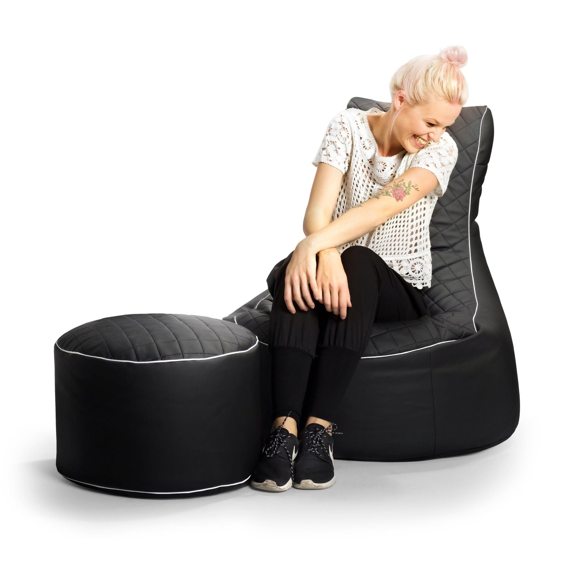 Woman sitting on a black bean bag chair with ottoman on a white background