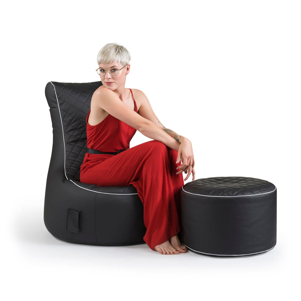 Woman in a red dress sitting on a black bean bag chair with ottoman on a white background