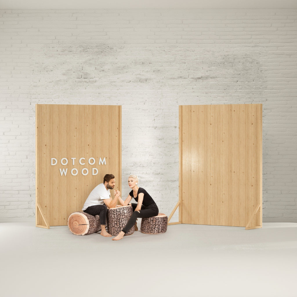 Two people sitting on wooden stools in front of two large wooden panels with 'Dotcom Wood' branding.