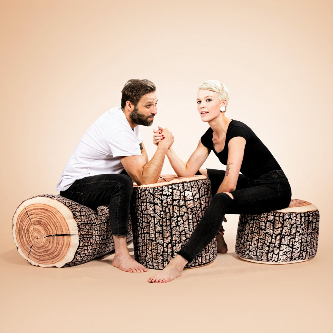 Two people sitting on tree stump stools against a beige background