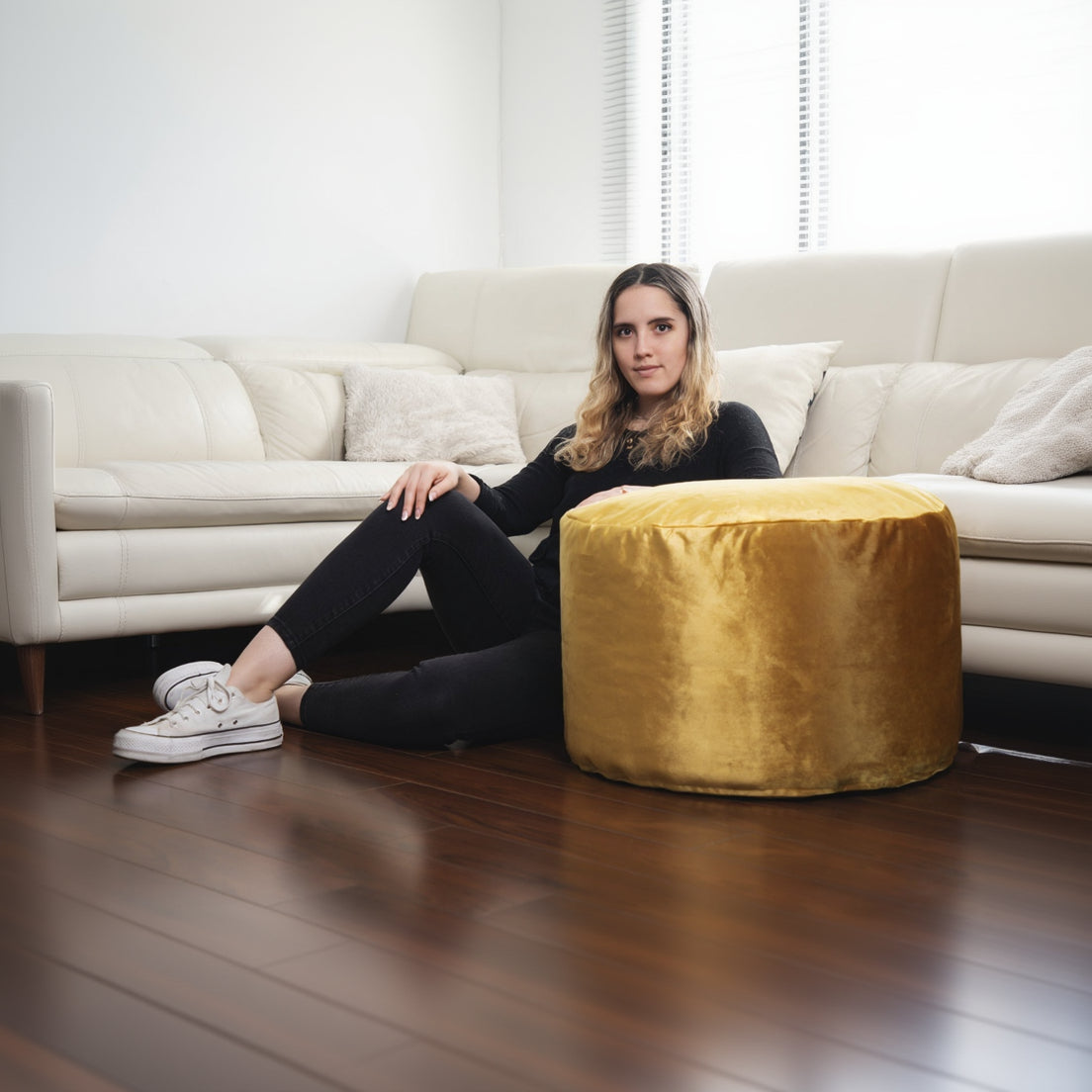 Woman sitting on a yellow pouf in a living room with a white sofa.