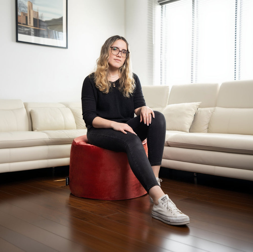 Woman sitting on a red ottoman in a living room.