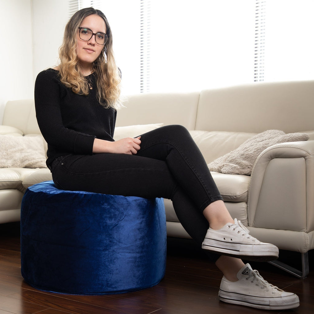Woman sitting on a blue ottoman in a living room.