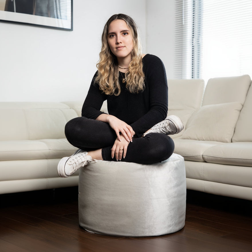 Woman sitting on a white ottoman in a living room.