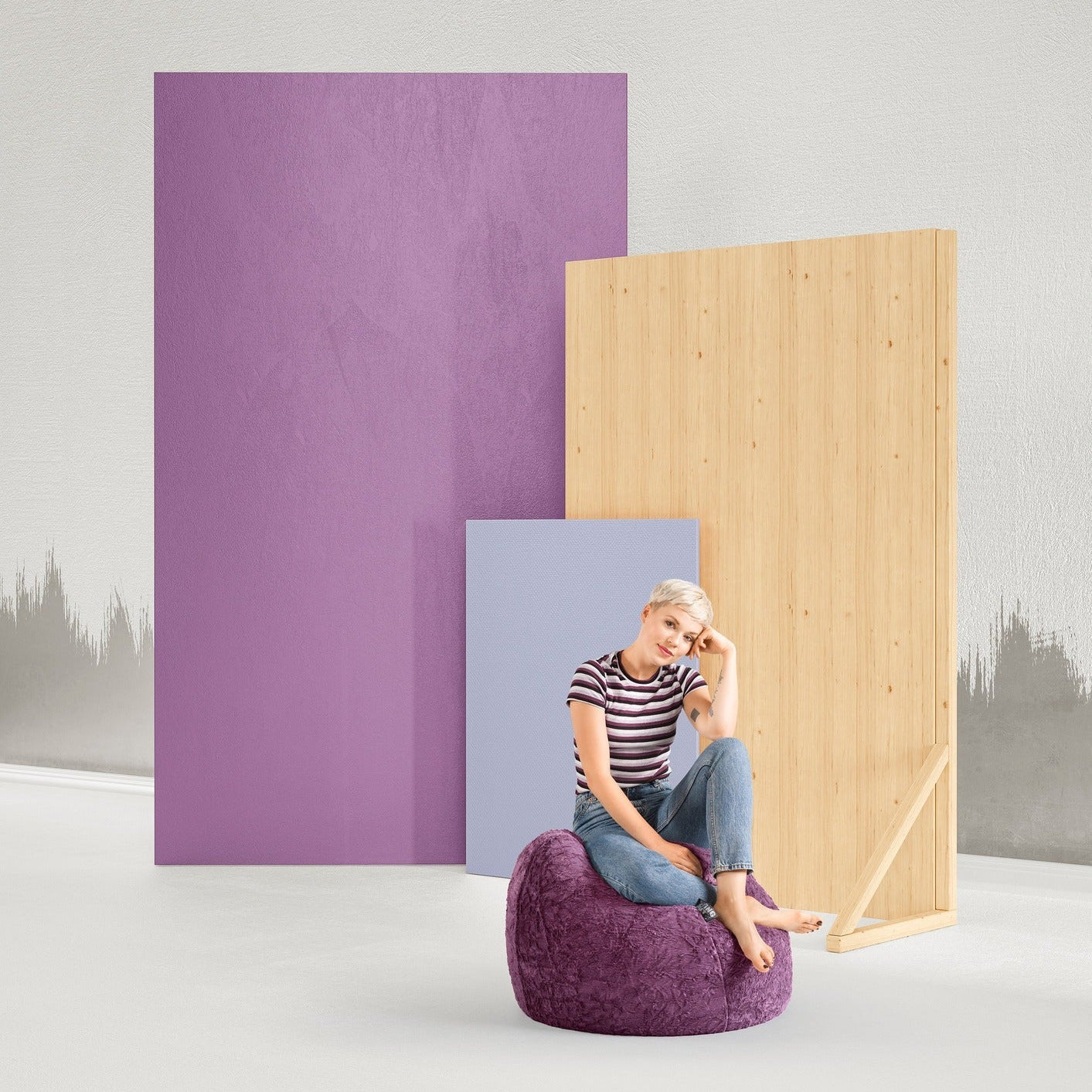 Woman sitting on a purple pouf in front of colorful panels against a white wall.