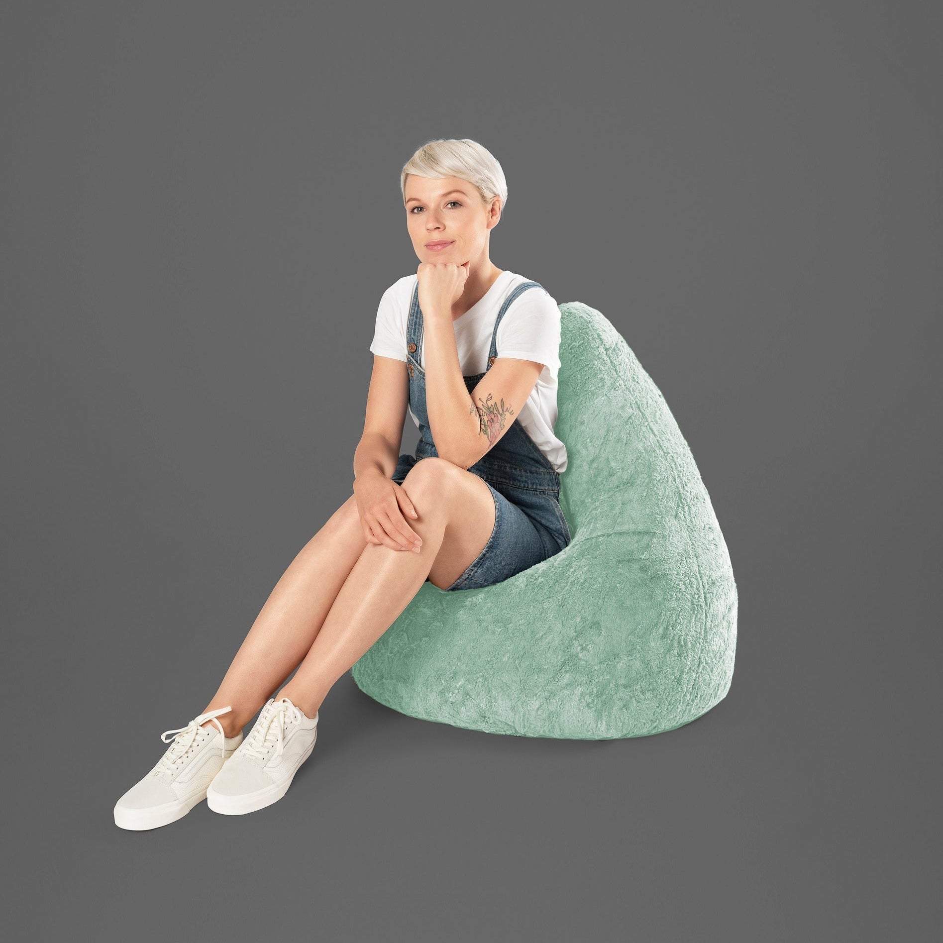 Person sitting on a green bean bag chair against a gray background