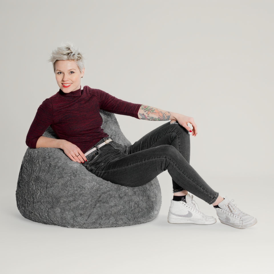 Woman sitting on a gray bean bag chair against a white background