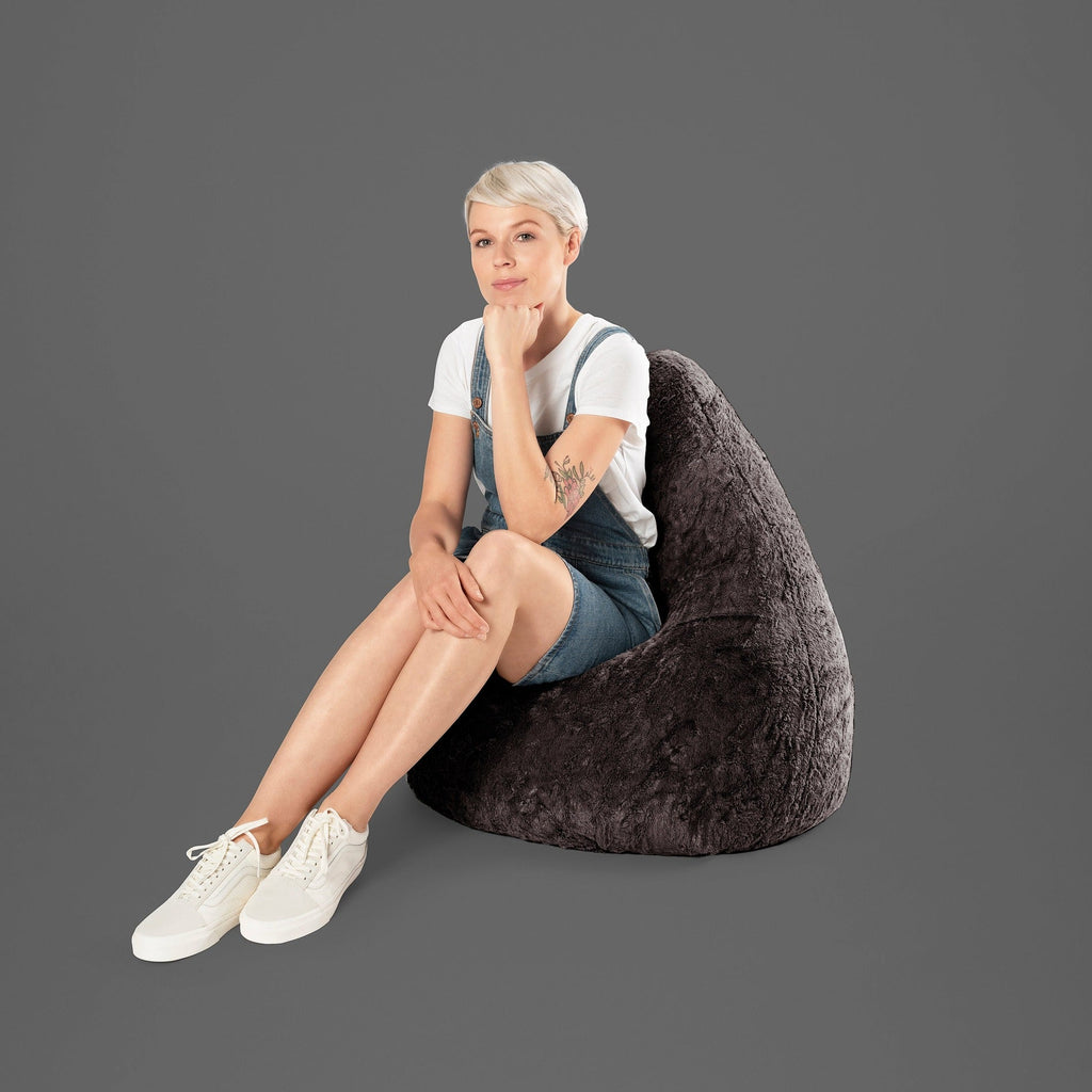 Woman sitting on a dark gray bean bag chair against a plain background