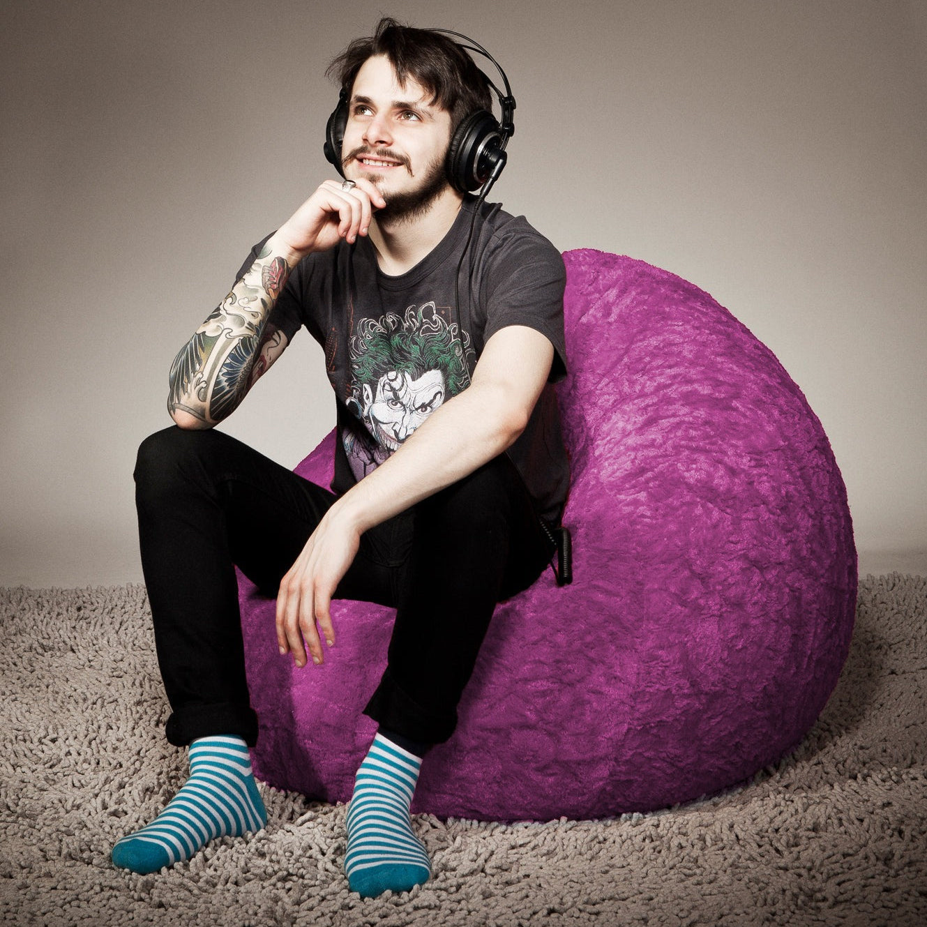 Man with tattoos sitting on a purple bean bag chair wearing headphones.