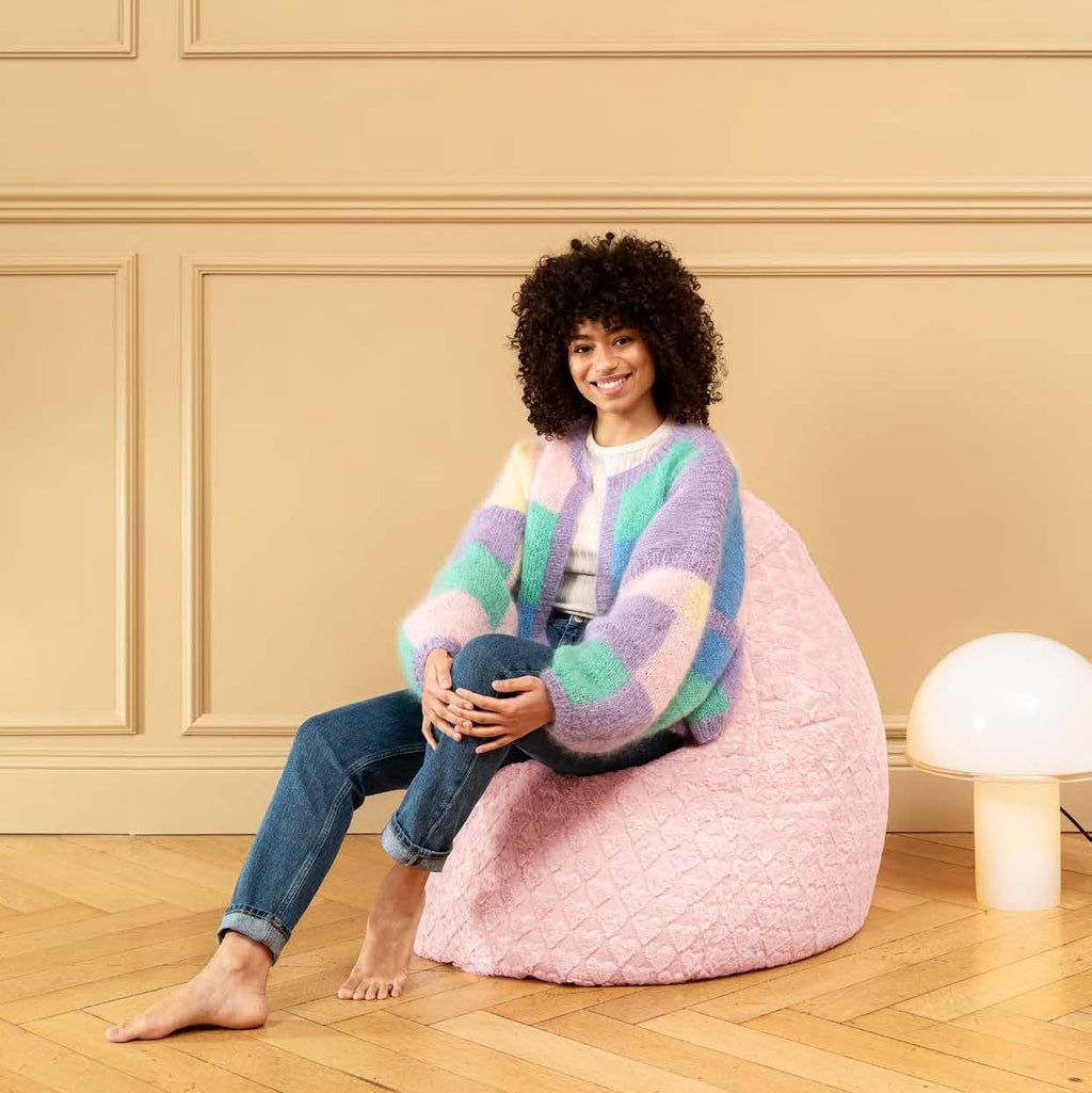 Woman sitting on a pink bean bag chair in a room with beige walls and wooden floor.