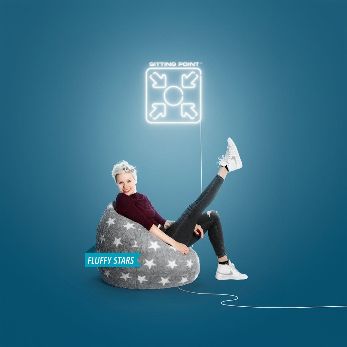 Person sitting on a gray bean bag chair with star patterns against a blue background, featuring the brand 'Sitting Point'.