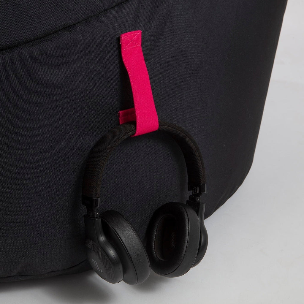 Black headphones hanging from a black bag with a pink strap on a light gray background