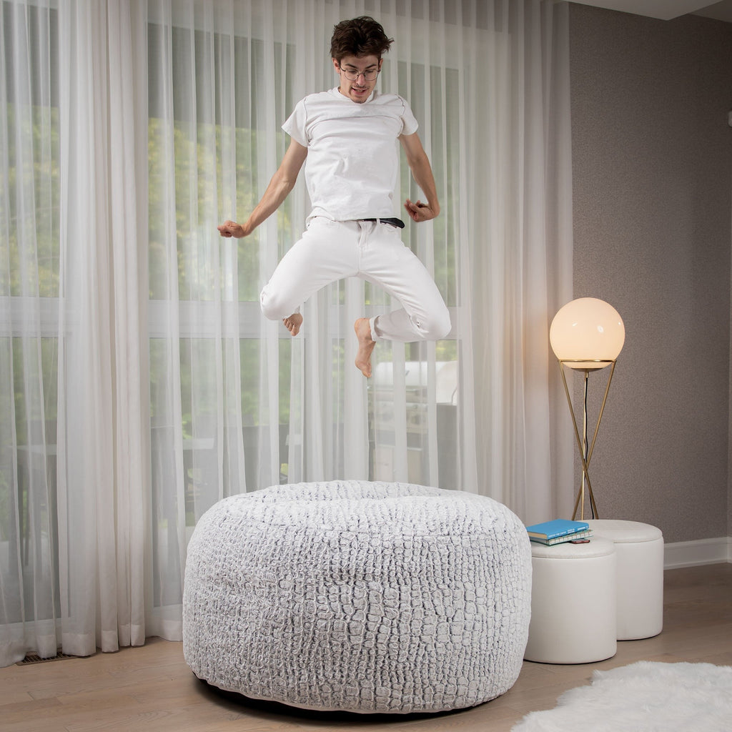Person jumping on a textured ottoman in a modern living room.