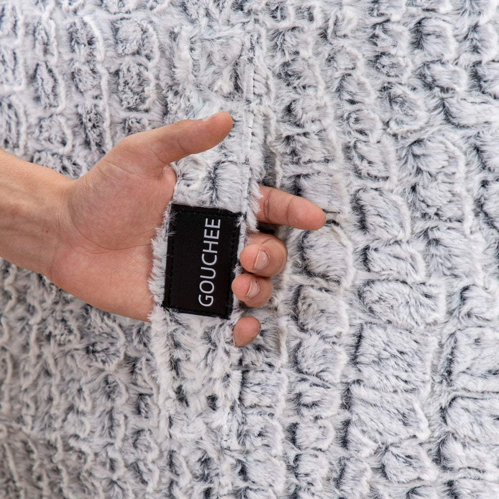 Hand holding a small black card with 'Gouchee' branding against a textured gray fabric background.