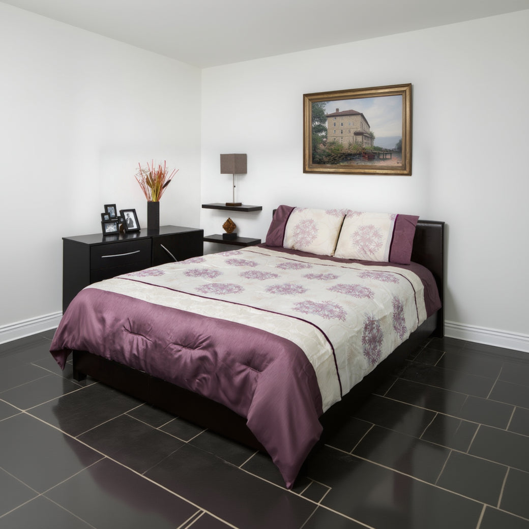 Bed with purple and white floral patterned bedding in a bedroom setting.