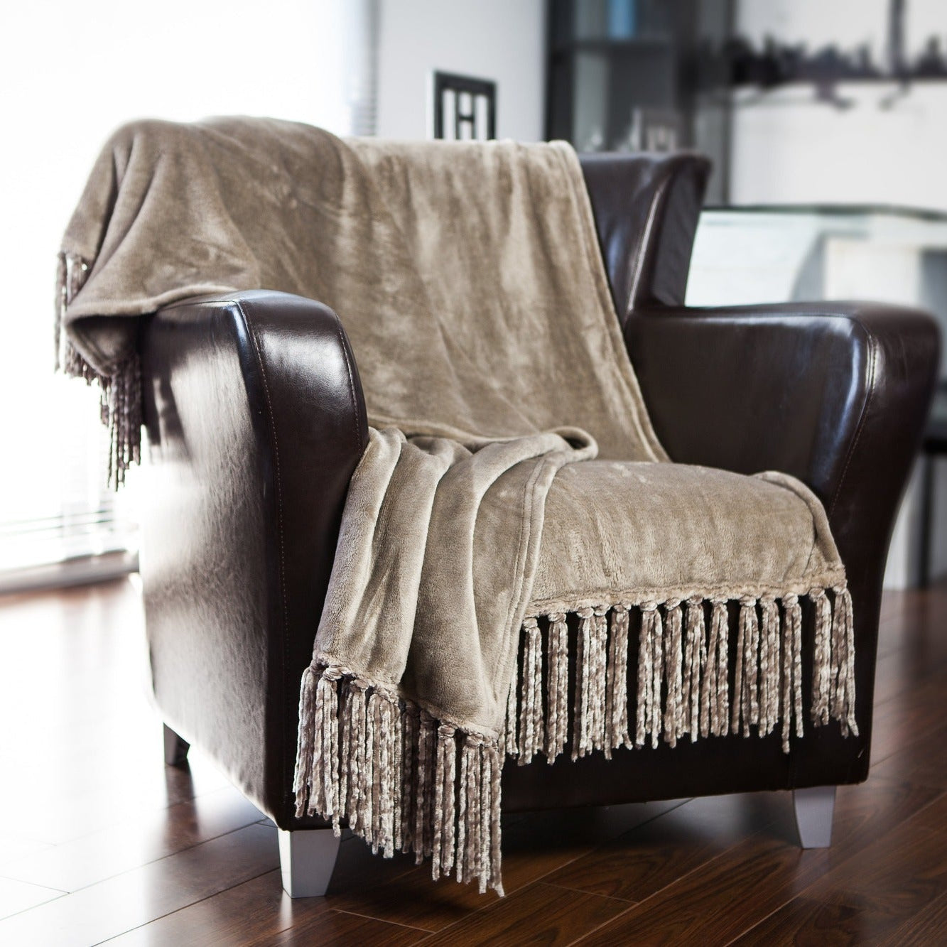 Brown textured blanket draped over a dark brown armchair in a room with wooden flooring.