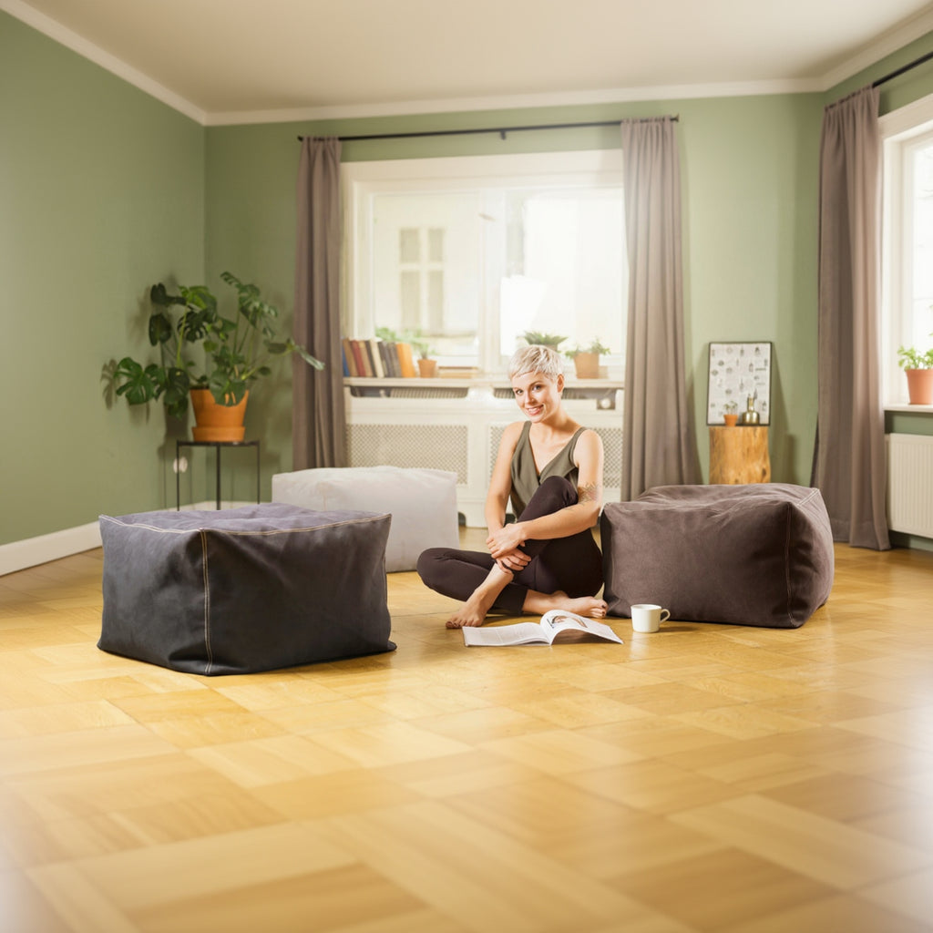 Woman sitting on a bean bag chair reading a book in a cozy living room.