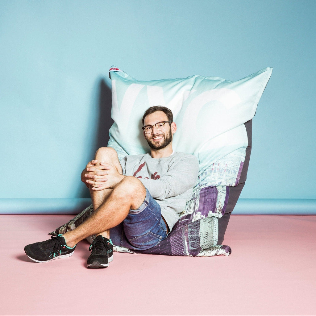 Man sitting on a large bean bag chair against a light blue wall.