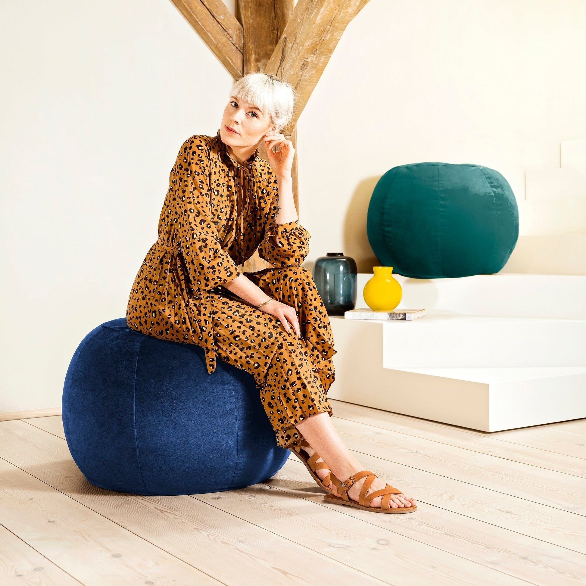 Woman in a leopard print dress sitting on a blue bean bag chair in a modern interior setting.