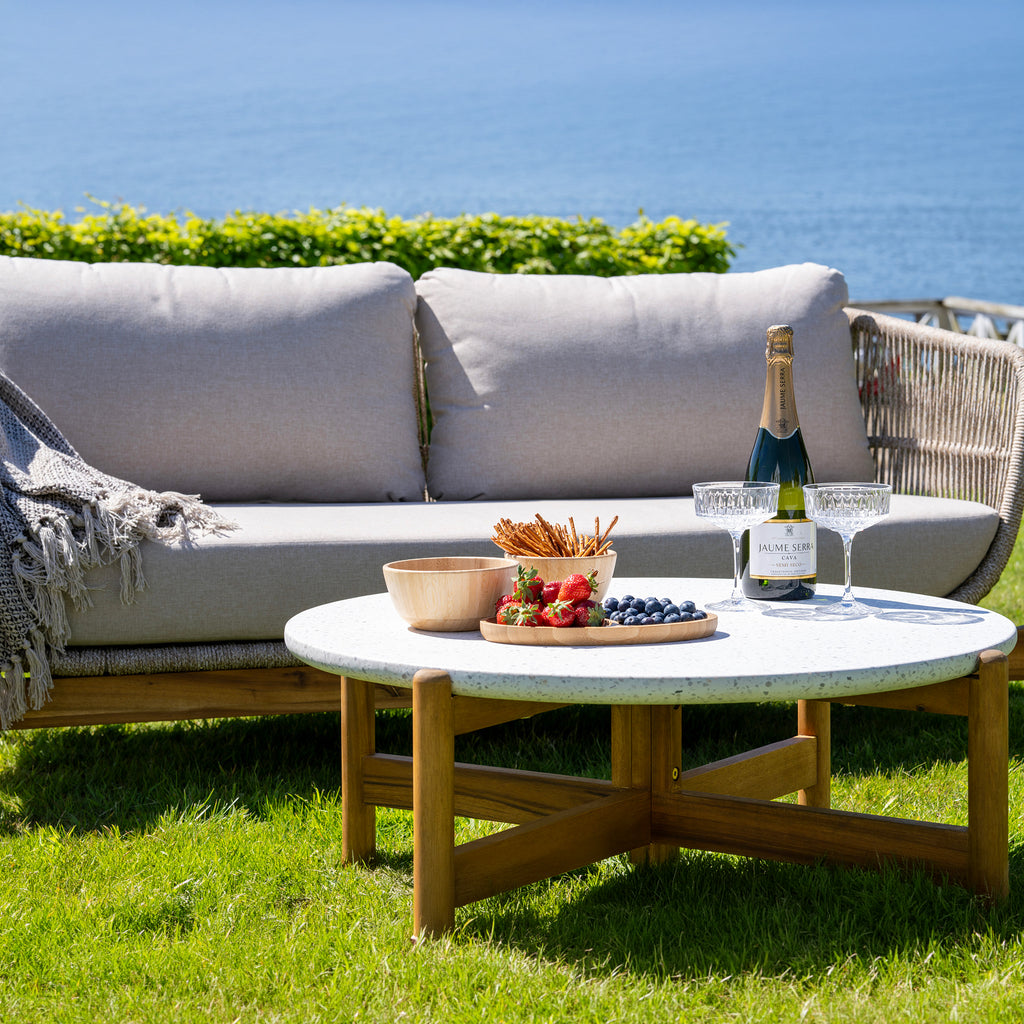 Outdoor setting with a sofa, table, and wine bottle by the sea.