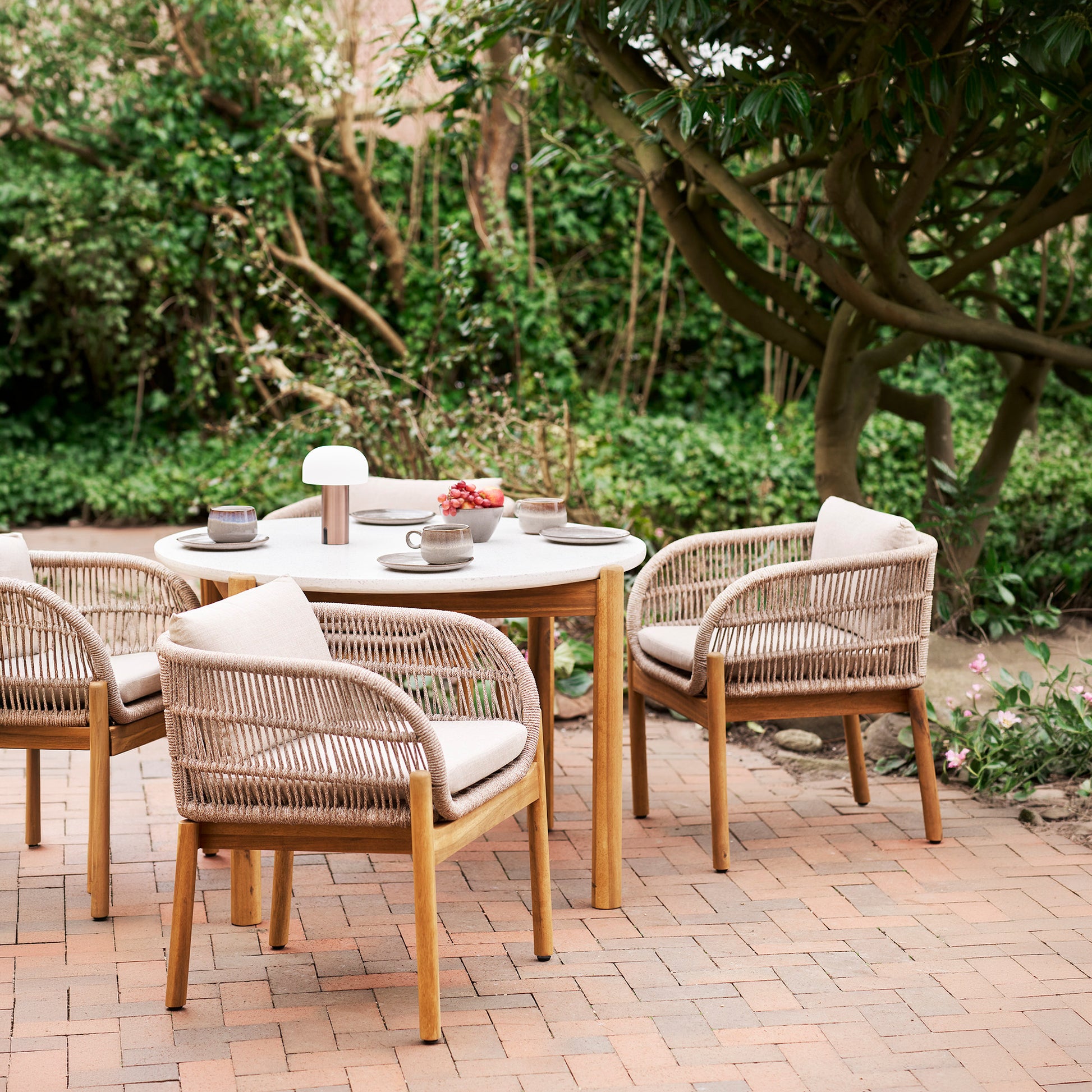 Portofino outdoor dining chairs in acacia wood and rope with beige cushions styled around dining table on outdoor patio