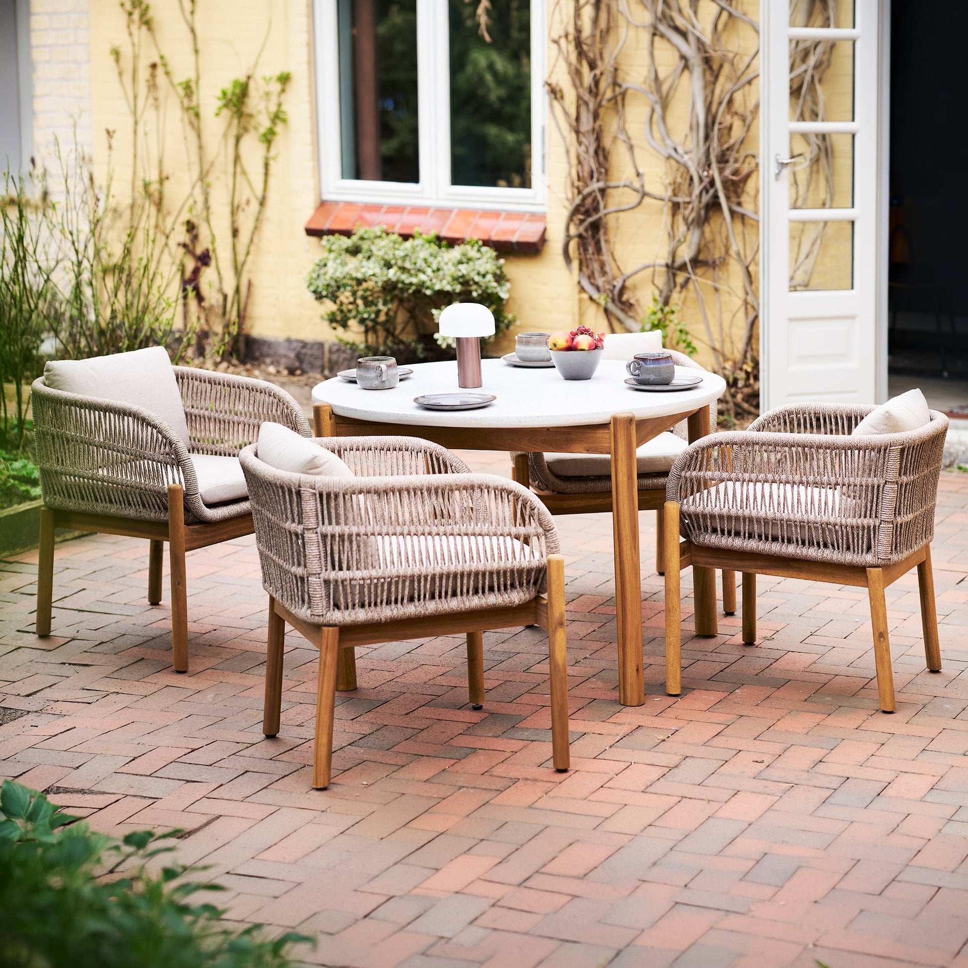 Portofino outdoor dining chairs in acacia wood and rope with beige cushions styled around dining table on outdoor patio