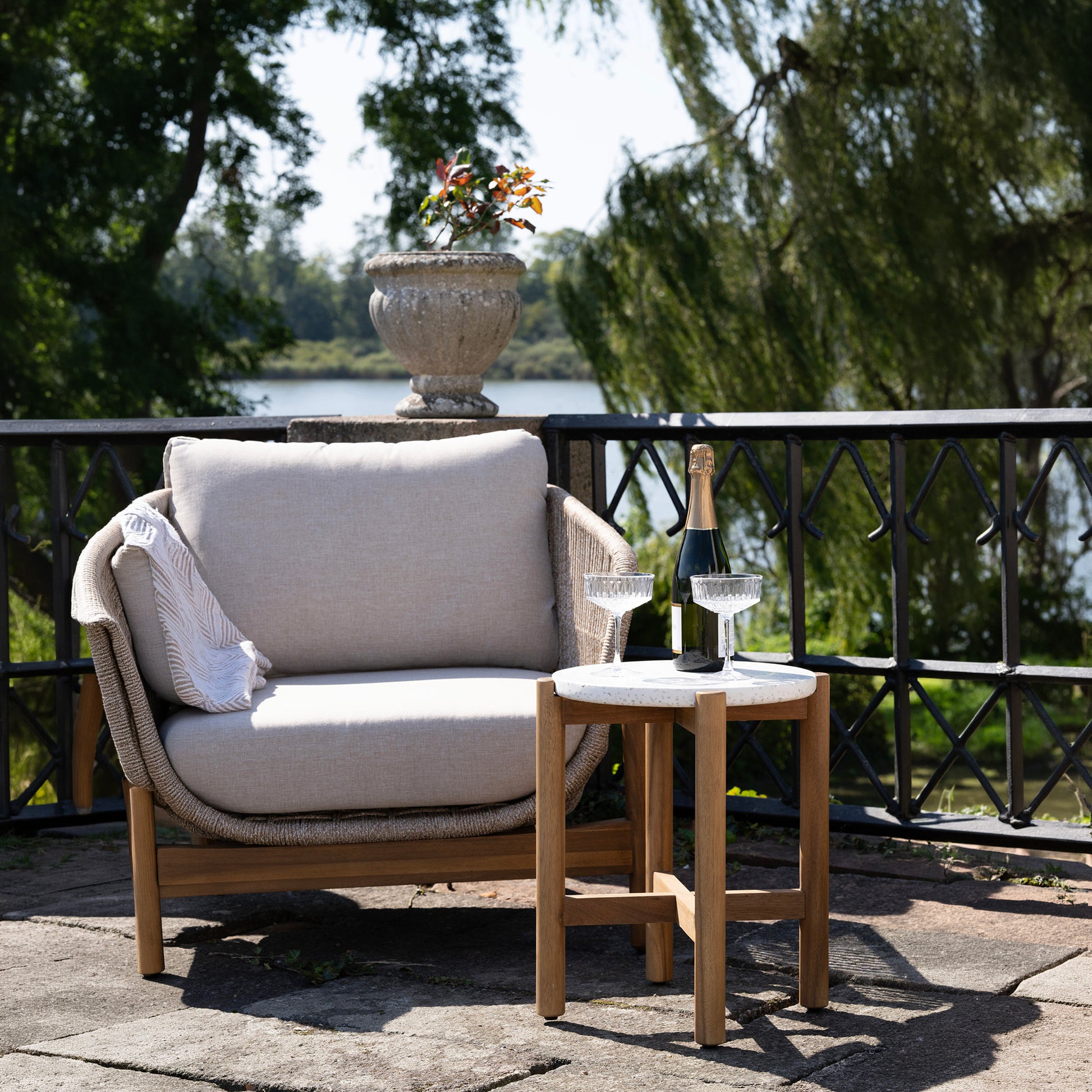 Outdoor furniture set with a chair and small table on a patio, featuring a bottle of champagne and glasses.