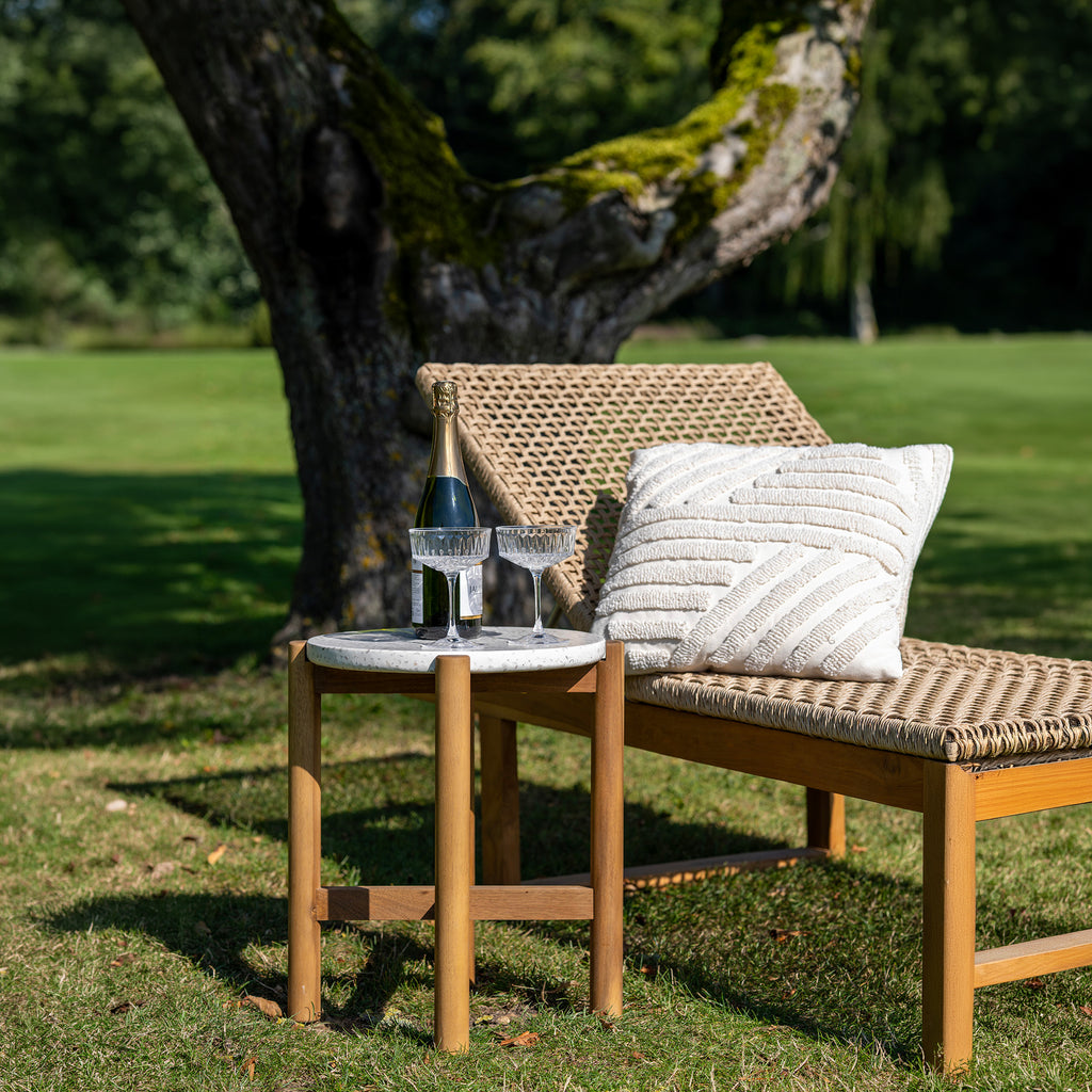 Wicker bench with a bottle and glasses on a small table in a grassy area.
