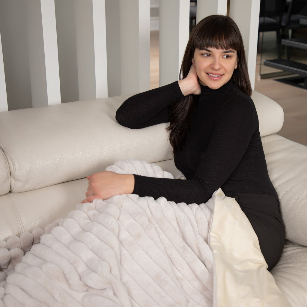 Woman sitting on a couch with a textured blanket, smiling at the camera.