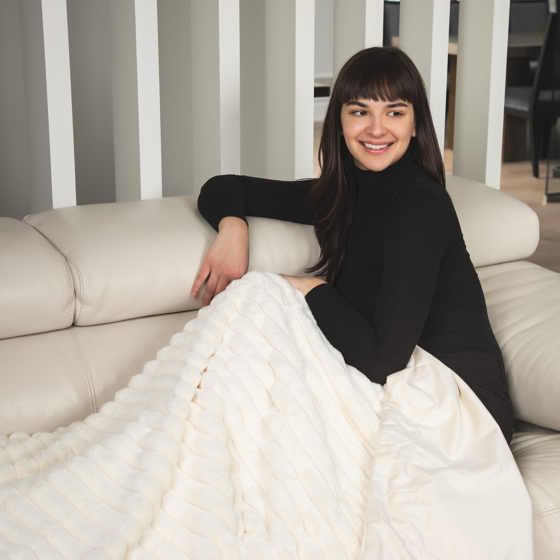 Woman sitting on a couch with a white blanket, smiling at the camera.