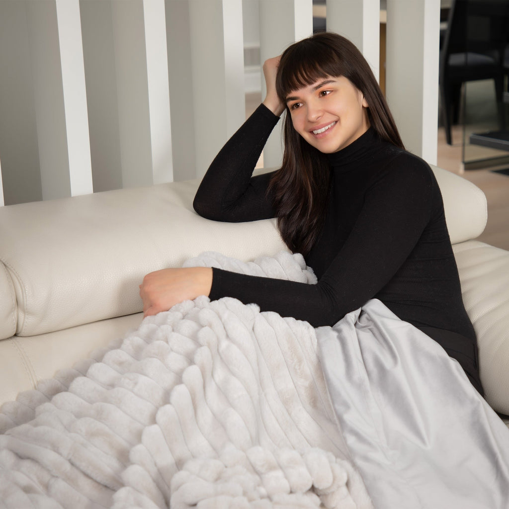 Woman sitting on a couch with a white blanket, smiling at the camera.