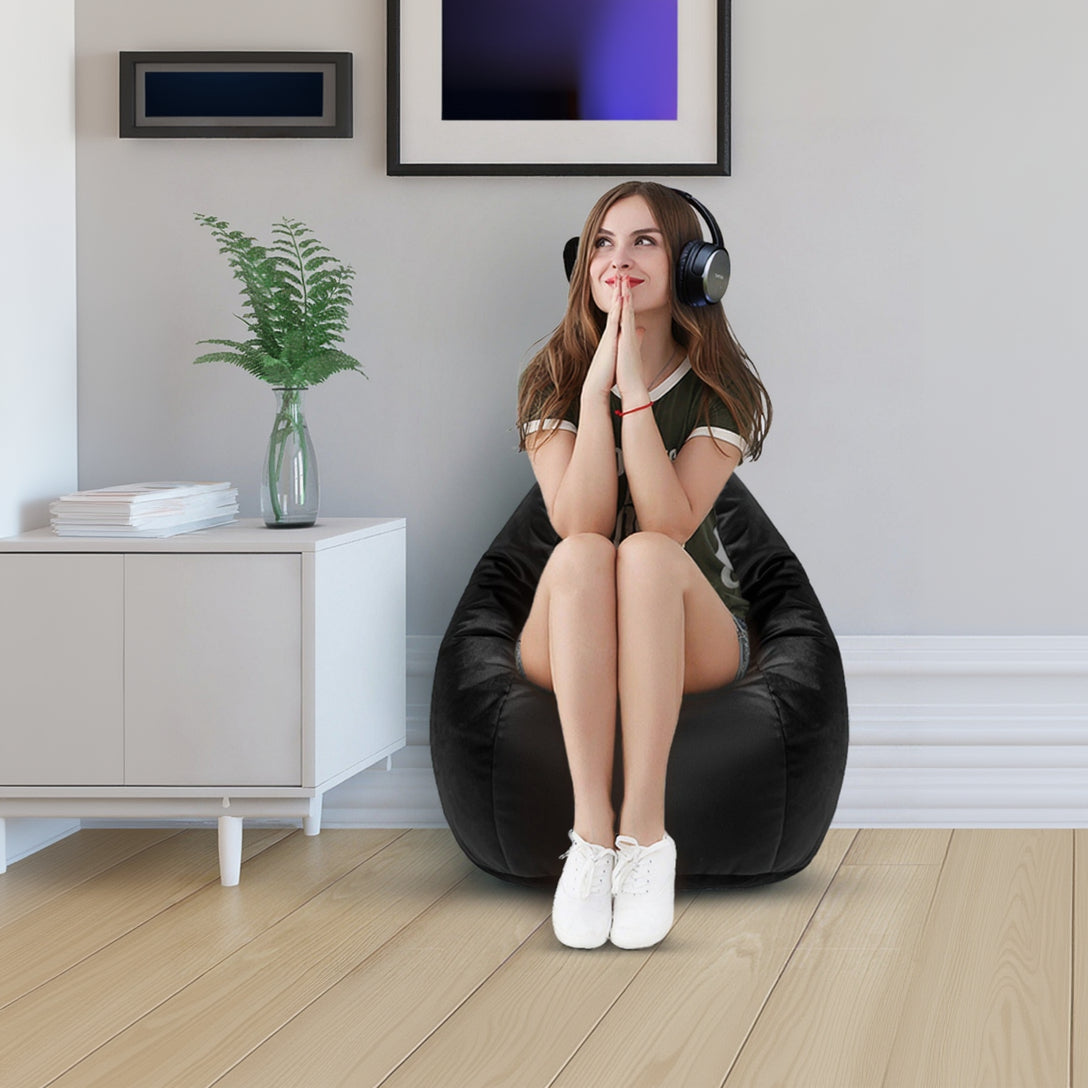 Woman sitting on a black bean bag chair wearing headphones in a room with a plant and framed pictures.