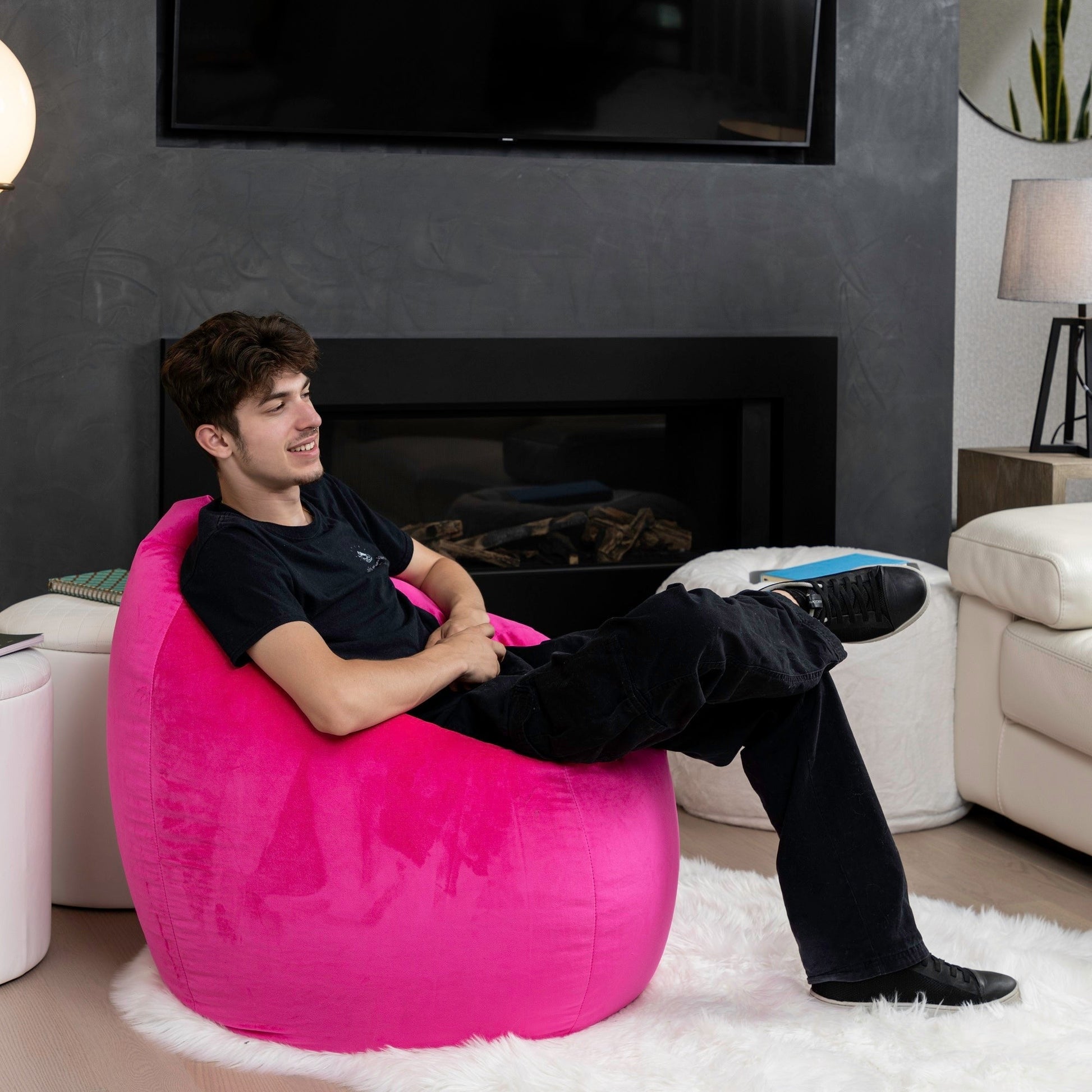 Man sitting on a pink bean bag chair in a living room with a fireplace.
