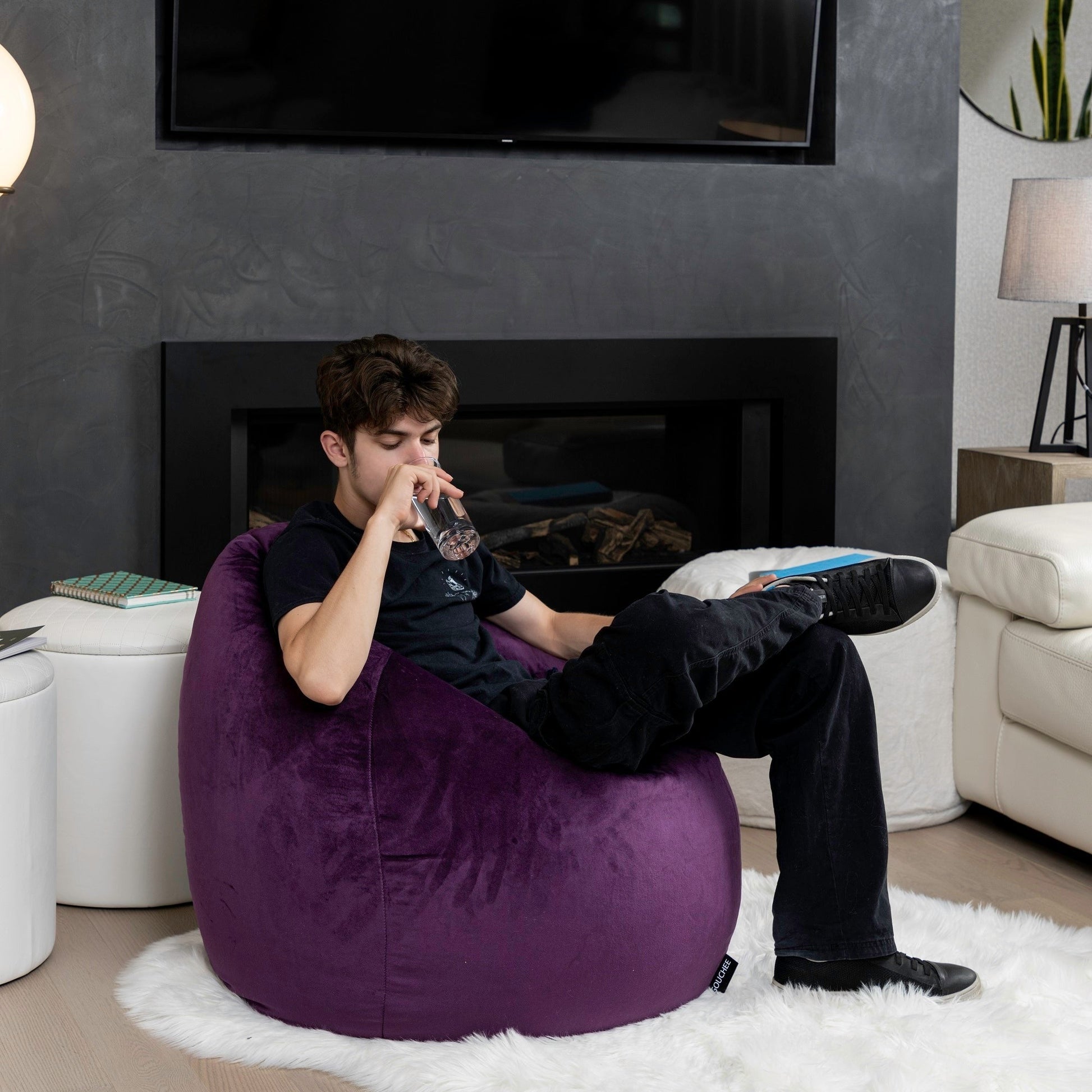 Man sitting on a purple bean bag chair in a living room with a fireplace and TV.