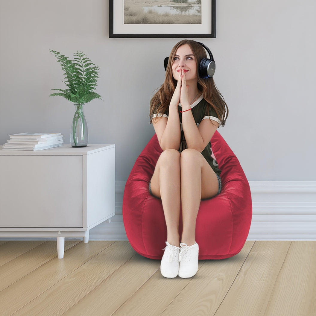 Woman sitting on a red bean bag chair wearing headphones in a room with a plant and framed pictures.