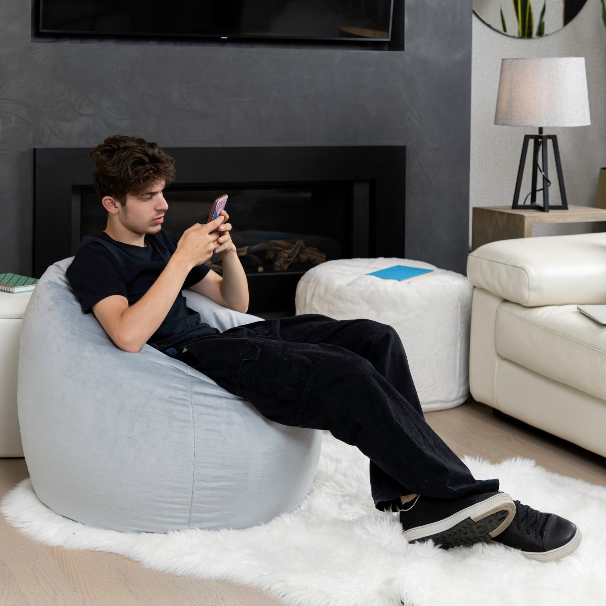 Man sitting on a bean bag chair using a smartphone in a living room.
