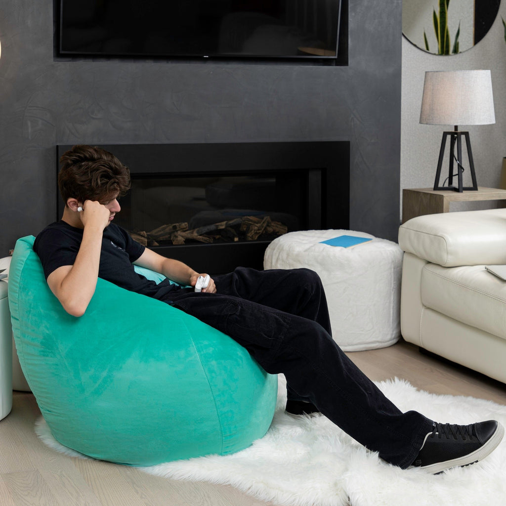 Person sitting on a teal bean bag chair in a living room with a fireplace and television.