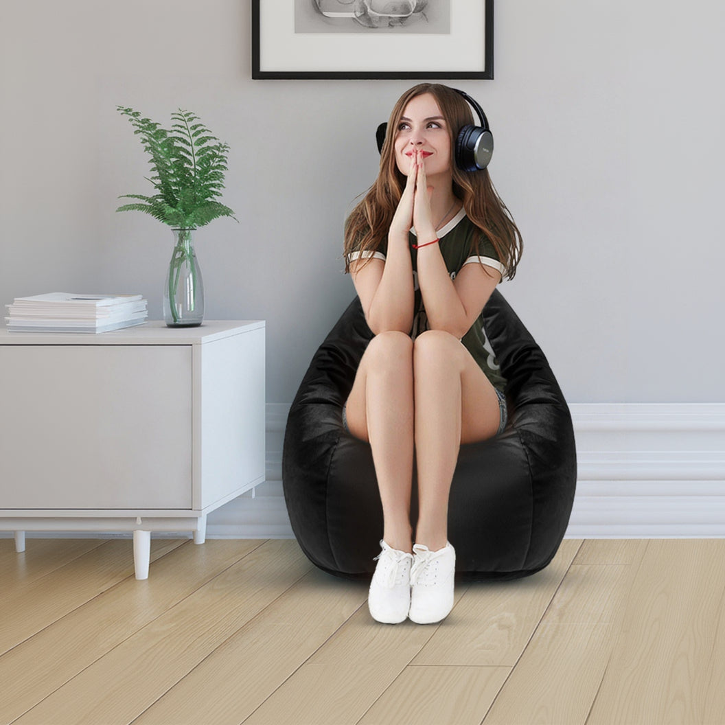 Woman sitting on a black bean bag chair wearing headphones in a room with a plant and framed pictures.