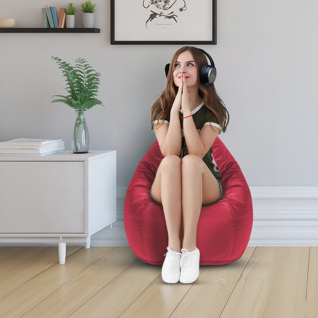Woman sitting on a red bean bag chair wearing headphones in a room with a plant and framed pictures.