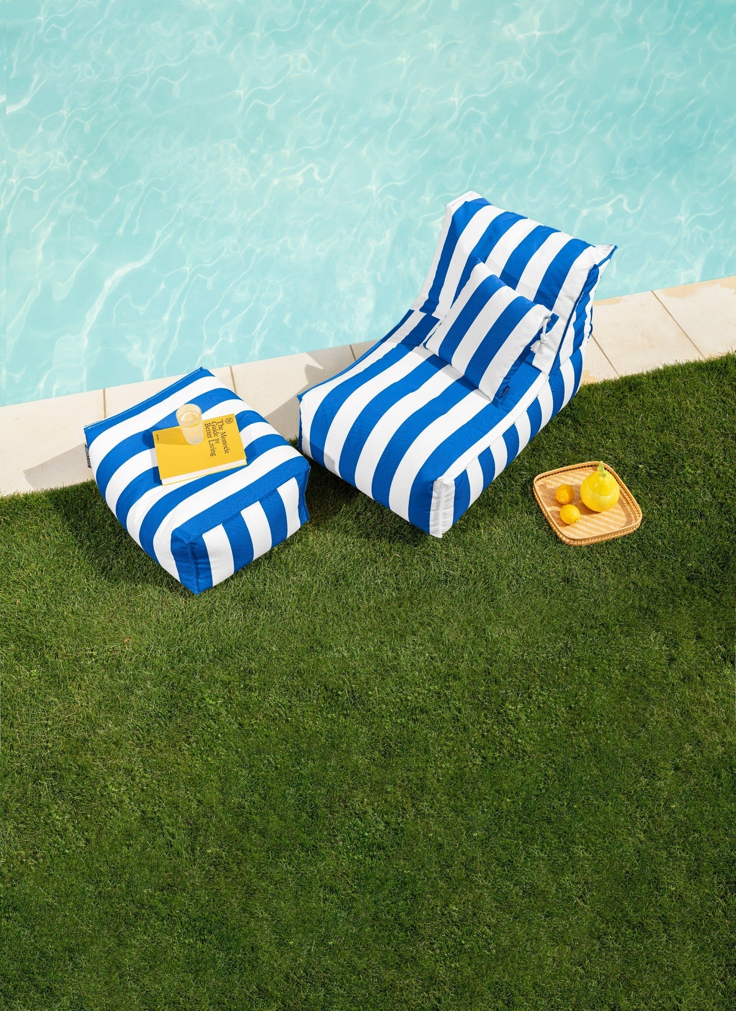 Blue and white striped inflatable lounge by a poolside with a small table and lemons.