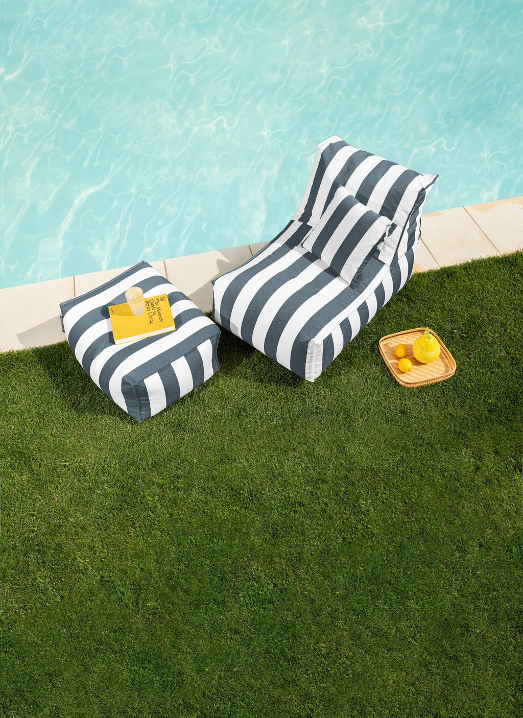 Two striped lounge chairs by a poolside with a small table and lemons.