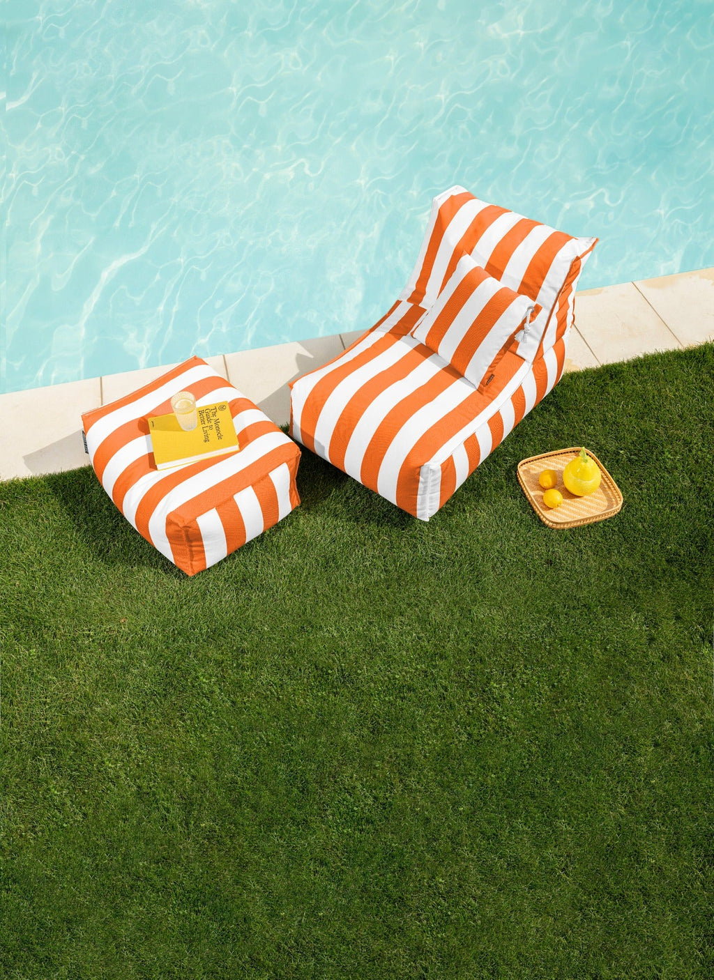 Orange and white striped lounge chairs by a poolside with snacks on a grassy area.