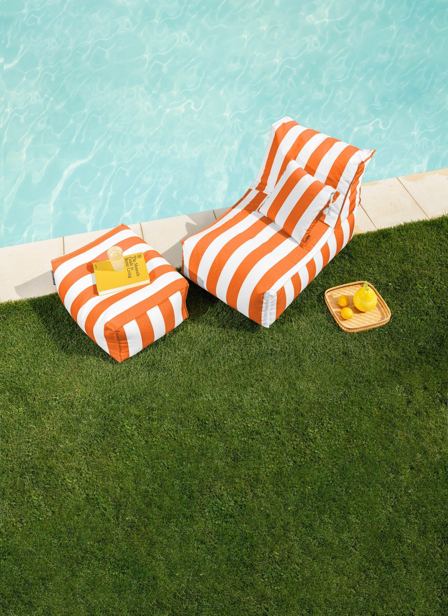 Orange and white striped lounge chairs by a poolside with snacks on a grassy area.