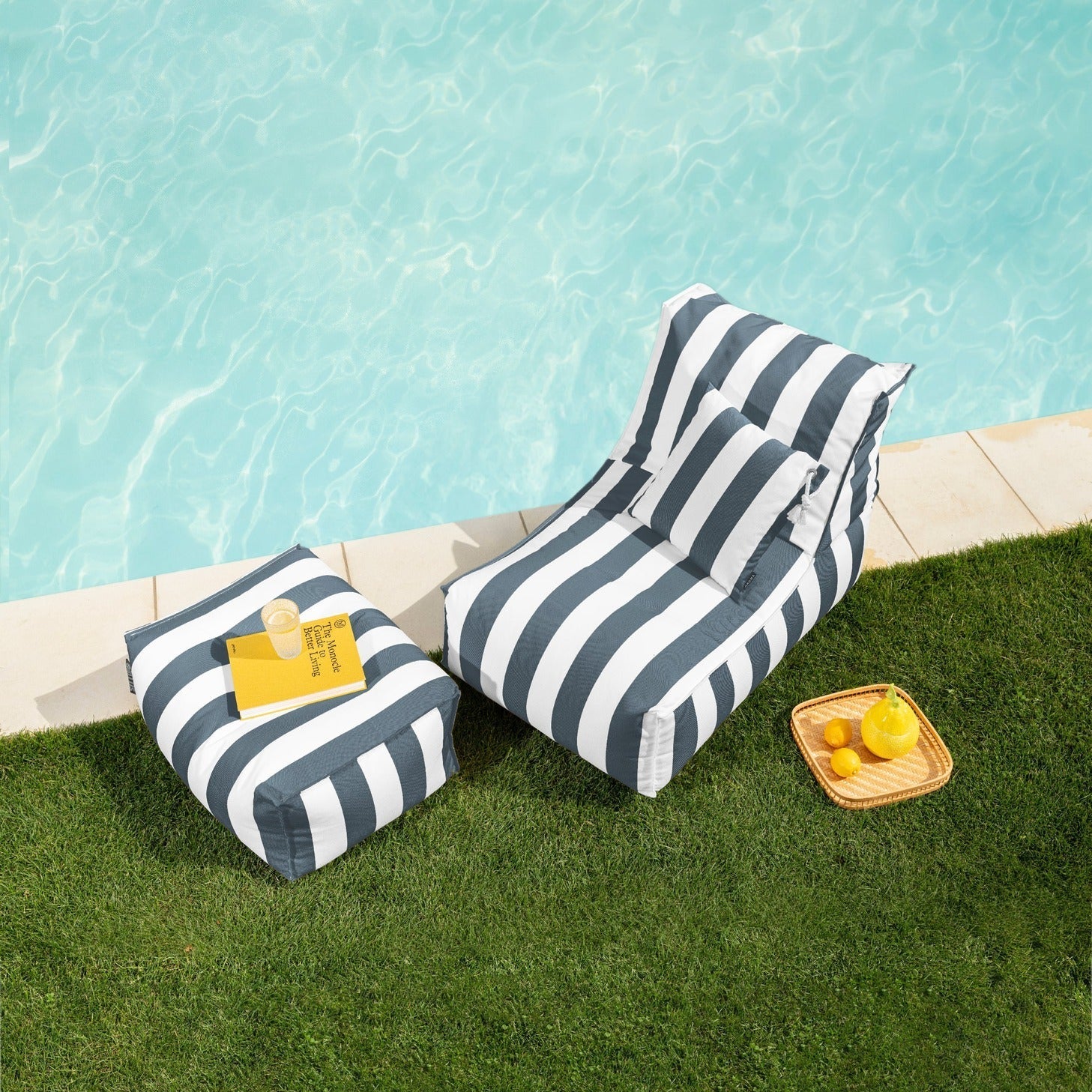 Two striped lounge chairs by a poolside with a small table and lemons.