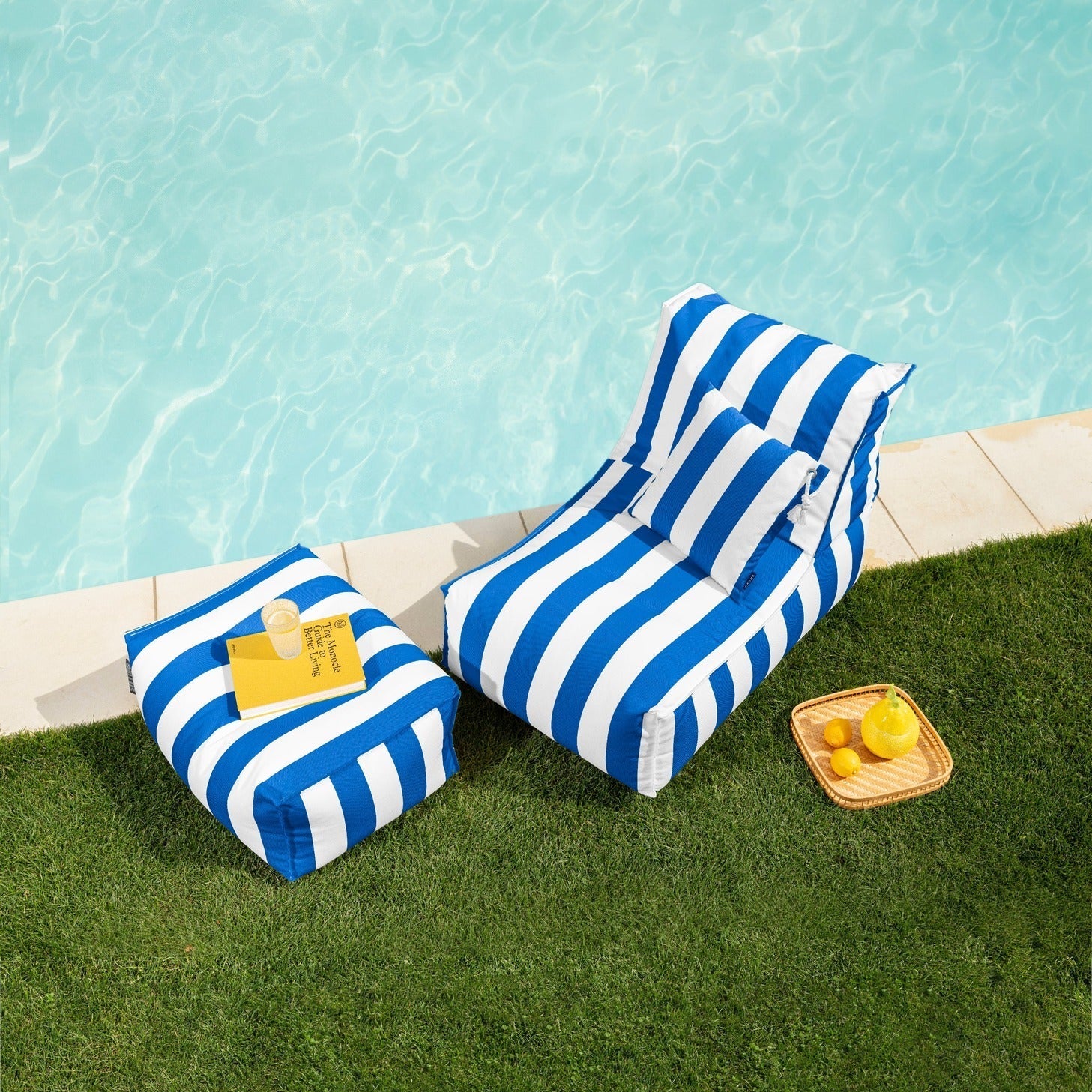 Blue and white striped inflatable lounge by a poolside with a small table and lemons.