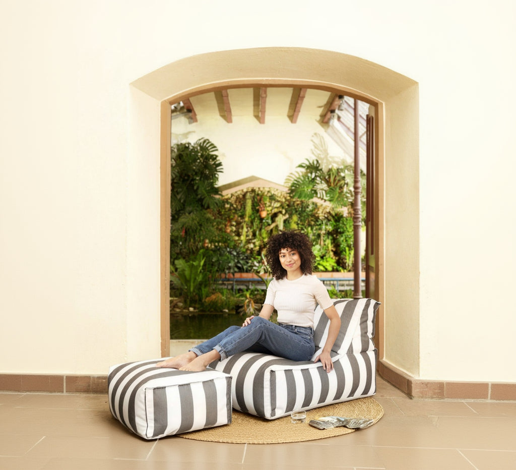 Woman sitting on a striped bean bag chair in a room with a large window view of greenery.
